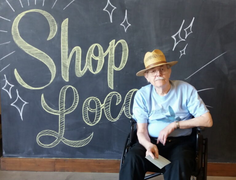 Bart Tendick sitting in front of a sign that says "Shop Loco"